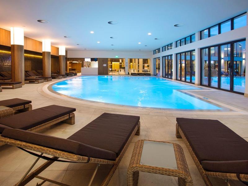 Área interior con piscina redonda, tumbonas y grandes ventanales en un hotel.