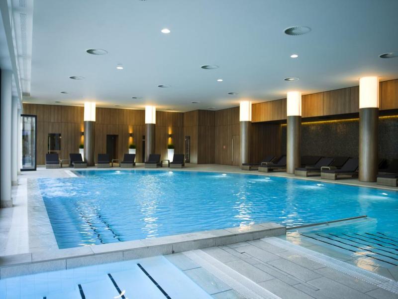 Área interior con una piscina rectangular grande y iluminación moderna en un hotel.