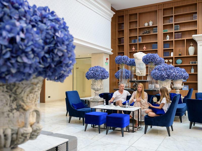 Salón de hotel con hortensias azules en macetas de piedra y huéspedes en mesas.