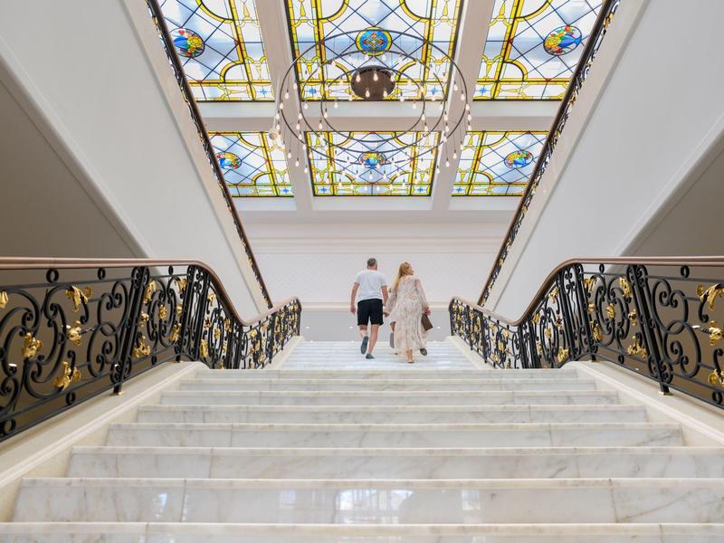 Escalera que conduce a una sala luminosa con techo de vidrio decorado en un hotel elegante.