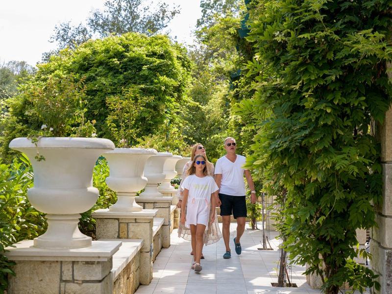 Pareja paseando por un camino bordeado de plantas verdes junto a grandes jarrones de piedra.