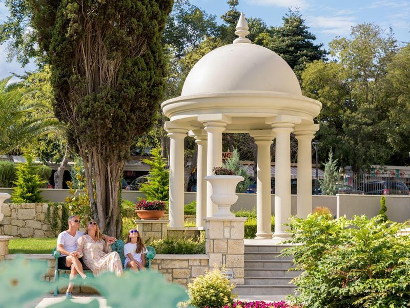 Un elegante área de piscina con un pabellón, rodeado de árboles y flores coloridas.
