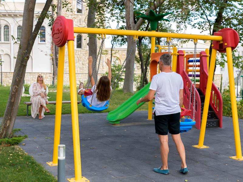 Un hombre observa a un niño jugando en un columpio colorido en un parque.