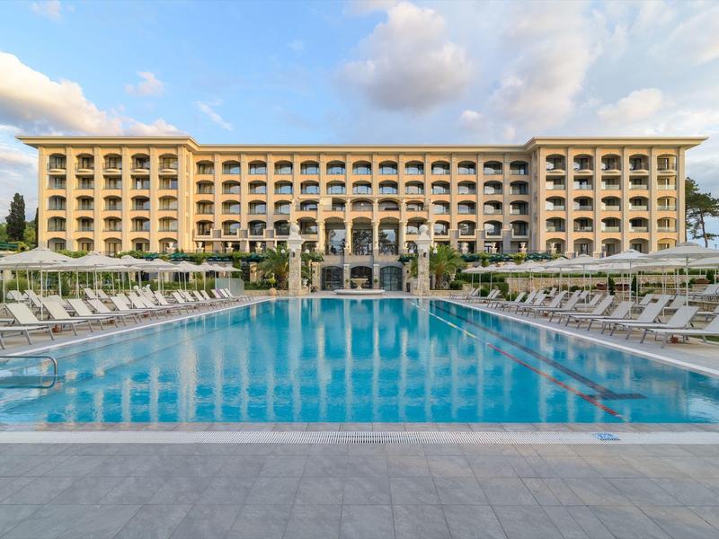 Complejo hotelero moderno con gran piscina exterior y tumbonas bajo un cielo azul.