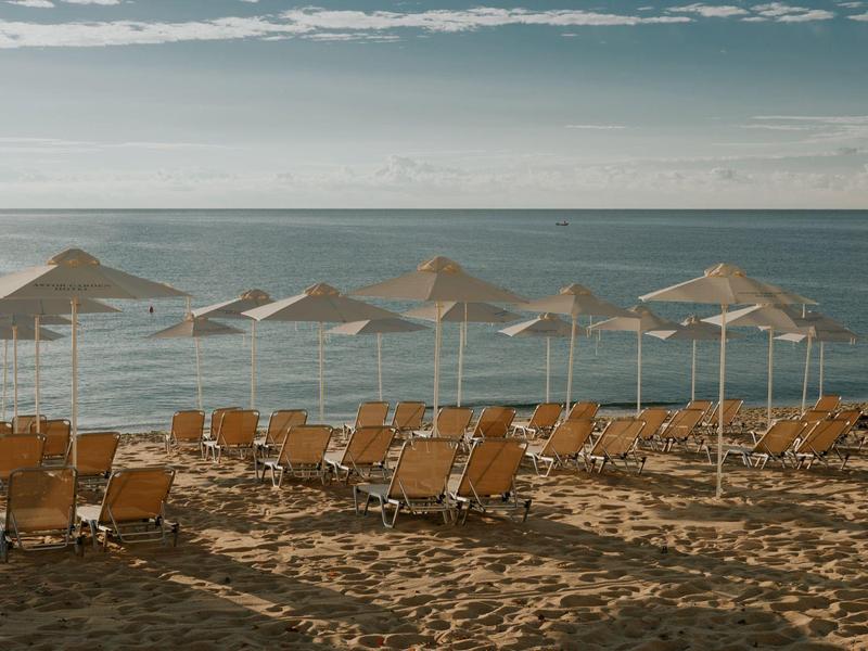 Sillas y sombrillas vacías en la playa de arena frente al mar tranquilo bajo cielo nublado.