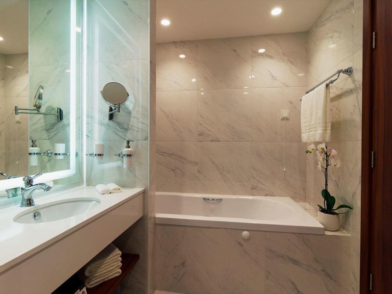 Baño moderno con bañera, lavabo, espejo iluminado y toallas en la pared.