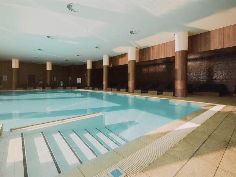 Piscina cubierta luminosa con escaleras y paredes de madera, ambiente tranquilo en un hotel.