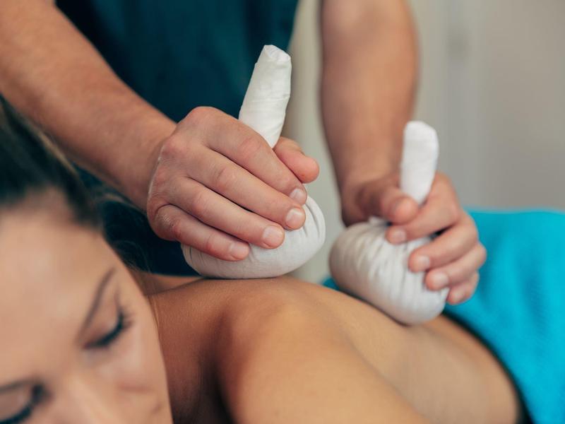 Mujer recibe un masaje con compresas de hierbas en la espalda en un spa.