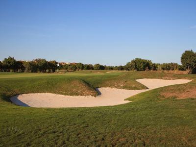 Zelené golfové hřiště s pískovými překážkami pod jasnou oblohou.