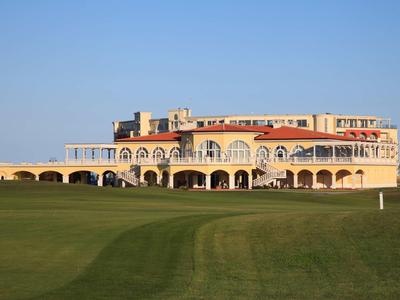 Large yellow hotel building with arches in front of a green lawn under a clear blue sky.