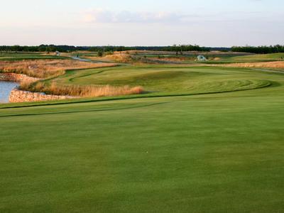 Green golf course field with water hazard and partly cloudy sky