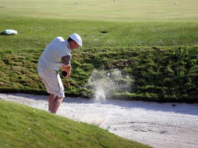 Golfista odpaluje míček z pískového bunkru na dobře udržovaném golfovém hřišti.