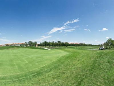 Wide, green golf course landscape under a blue sky with some clouds.