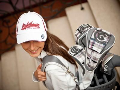 Woman wearing white cap and carrying golf equipment down the stairs.