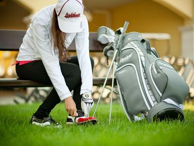Golfer tying her shoes beside a golf bag with clubs before teeing off.