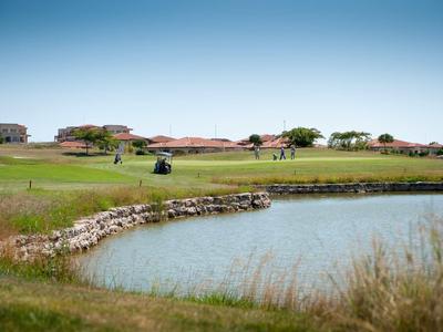 Zelené golfové hřiště s jezírkem a klubovnou pod jasnou oblohou