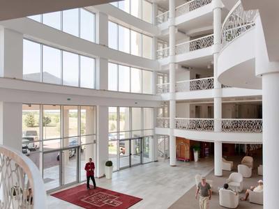 Světlá, moderní hotelová lobby s velkými okny a bílým interiérovým designem.