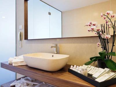 Moderní umývací prostor s obdélníkovým zrcadlem, nádobovým umyvadlem a orchidejí v hotelové koupelně.