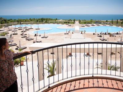 View from a balcony overlooking a large pool area with sun loungers and the sea in the background.