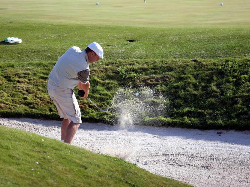 Golfista odpaluje míček z pískového bunkru na dobře udržovaném golfovém hřišti.