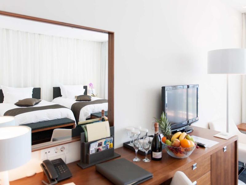 Moderní hotelový stolek s velkým zrcadlem, televizí a košíkem ovoce.