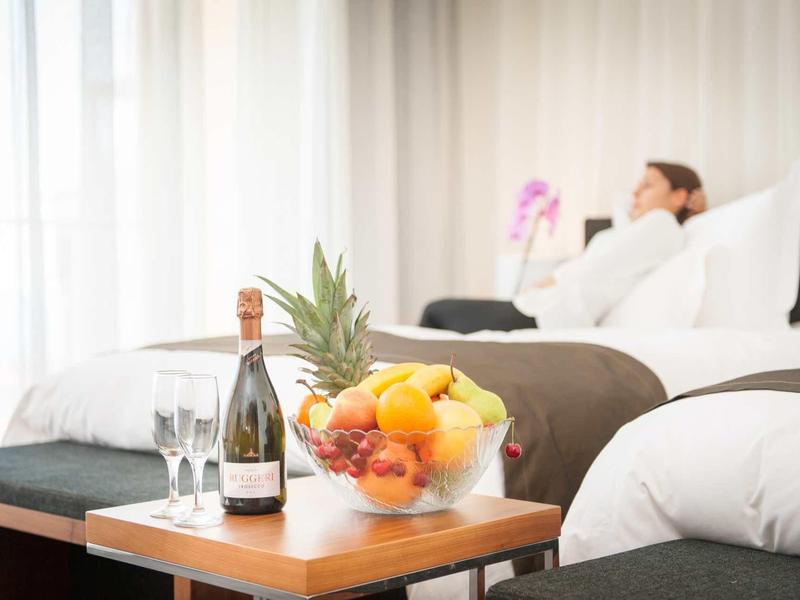 Čerstvé ovoce a šampaňské na stole před útulnou postelí v hotelovém pokoji.