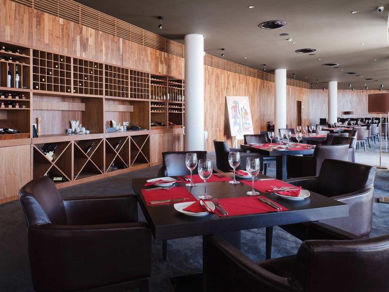 Elegantní restaurace s moderním dřevěným interiérem a stoly prostřenými s červenými akcenty.