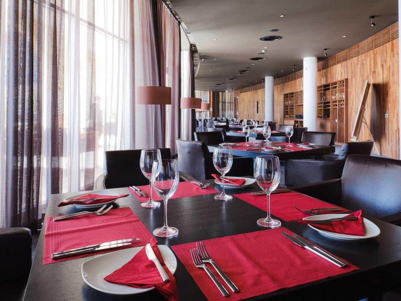 Elegantní restaurace s černo-červeným prostřením a velkými okny se závěsy.