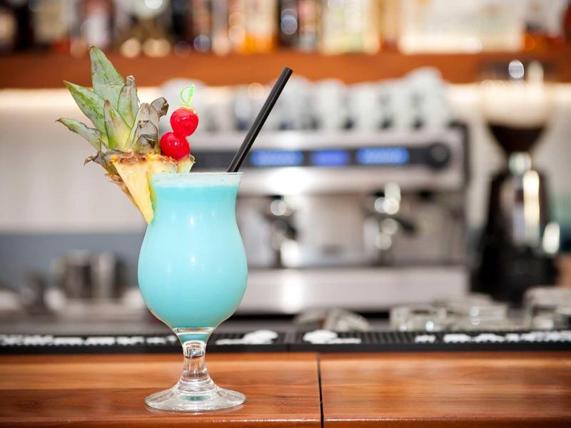 Modrý koktejl s ananasem a třešněmi ve sklenici u baru.