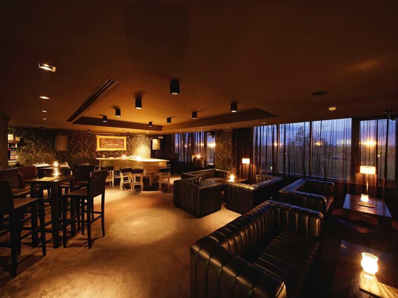 Pohodlný hotelový bar s koženými sedačkami, barem a večerním ambientním osvětlením.