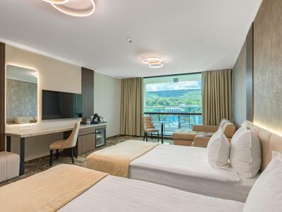 Camera d'hotel moderna con due letti, scrivania, TV e balcone con vista sulle montagne.