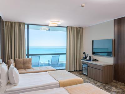 Camera d'hotel con due letti, balcone e vista mare attraverso grandi finestre di vetro.