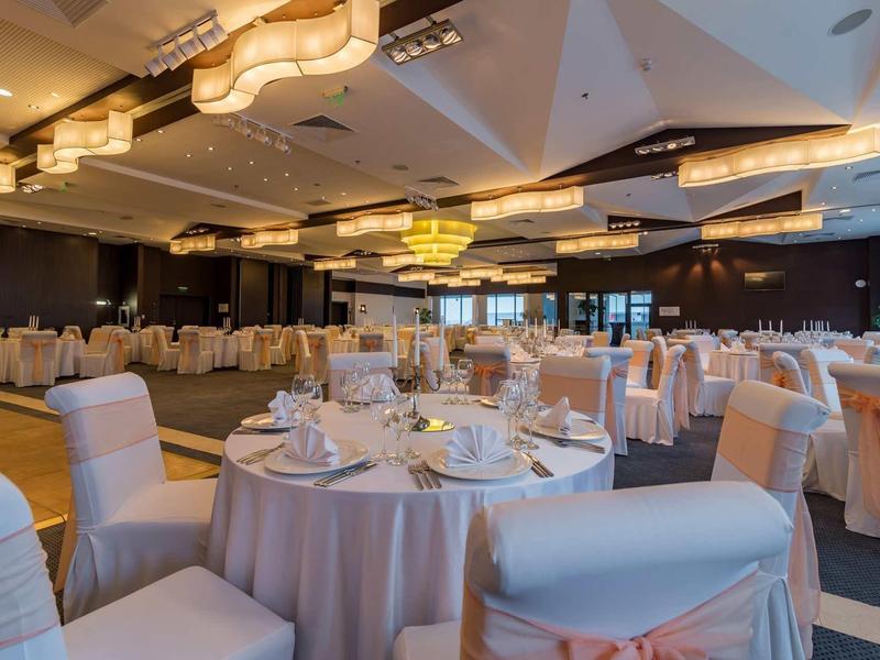 Grande salle de banquet avec des tables rondes dressées et des chaises élégamment décorées.