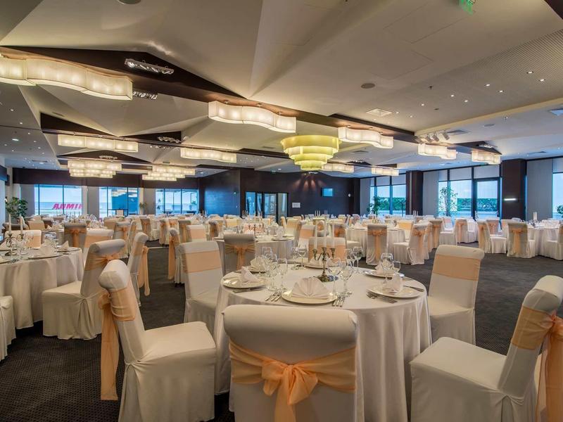 Salle de banquet élégante avec des tables rondes dressées et des chaises blanches avec des nœuds beiges.