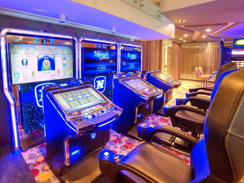 Plusieurs machines à sous avec éclairage bleu et fauteuils en cuir confortables dans une salle de jeux d'hôtel.