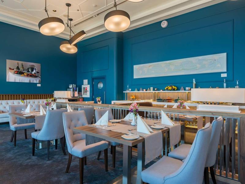 Restaurant élégant avec murs bleus, chaises grises et tables dressées dans un hôtel.