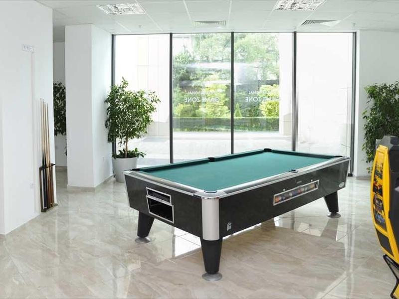 Salle de jeux lumineuse avec table de billard, bornes d'arcade et vue panoramique sur le jardin.