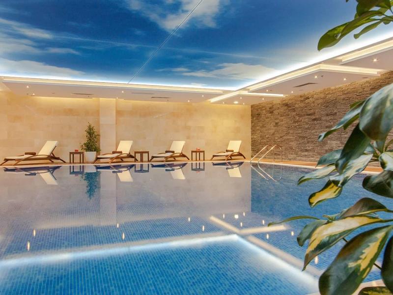 Piscine intérieure luxueuse avec chaises longues et éclairage indirect au plafond.