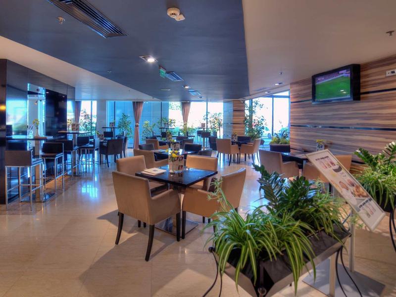 Restaurant d'hôtel moderne avec tables, chaises et plantes vertes dans un cadre lumineux.
