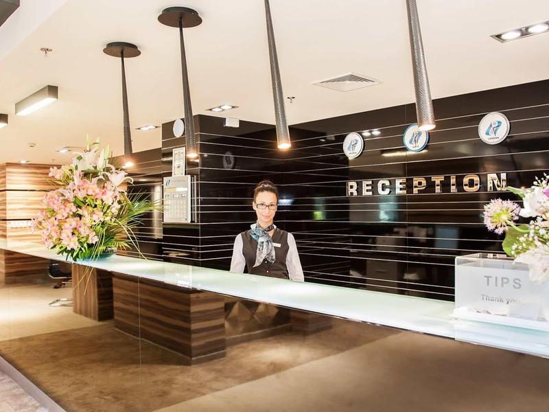 Réception d'hôtel avec comptoir, compositions florales et personnel dans un espace bien éclairé.