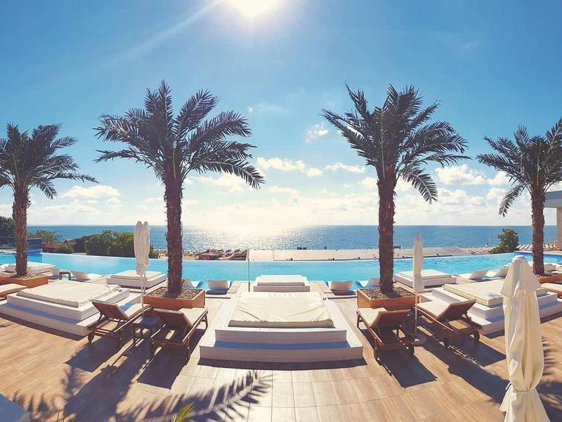 Plage ensoleillée avec palmiers, transats et mer calme sous un ciel bleu.