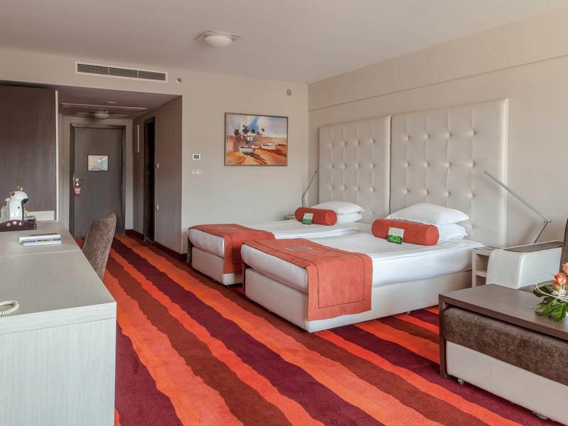 Chambre d'hôtel avec deux lits simples, moquette orange-rouge et mobilier moderne.