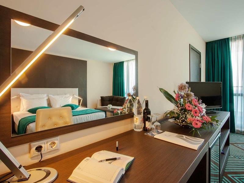 Bureau moderne de chambre d'hôtel avec miroir, bouquet de fleurs et télévision, lumière du jour par la fenêtre.