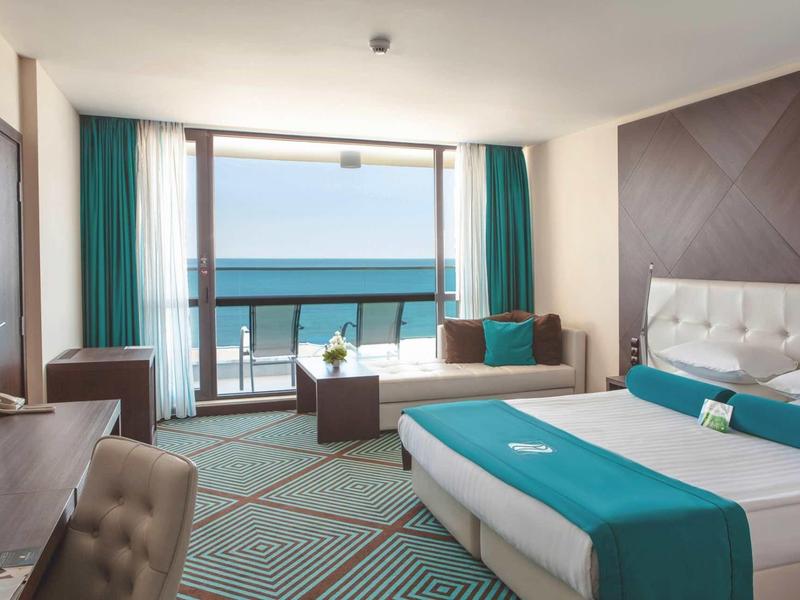 Chambre d'hôtel lumineuse avec lit double et vue sur la mer depuis le balcon.