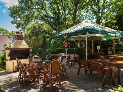 Accogliente area esterna con posti a sedere e barbecue sotto gli alberi in una giornata di sole.