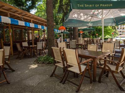 Freiluft-Café mit Holztischen, Stühlen und Sonnenschirmen in grüner, schattiger Umgebung.