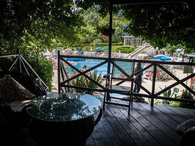 Überdachte Terrasse mit Holzboden und Gartenmöbeln, Blick auf Sonnenschirme und Bäume im Hintergrund.
