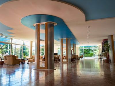 Großer, heller Raum mit blauen Deckenakzenten, Säulen und Sesseln, glatter Boden und viel Tageslicht.