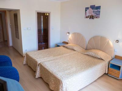 Ein helles Schlafzimmer mit zwei Betten, blauen Sesseln und einem Nachttisch mit Lampe.