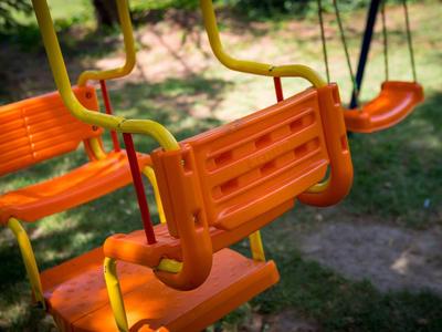 Mehrere orangefarbene Schaukelsitze aus Kunststoff an gelben Metallgestellen im Freien.